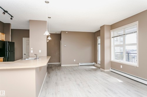 Open-concept living space with light wood-finish flooring, neutral wall tones, and a large window - 1-402 4245 139 Avenue, Edmonton, AB - Indoor Photo Showing Other Room