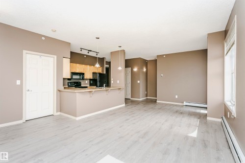 Open-concept living area featuring light wood-finish flooring, neutral wall tones, and a kitchen island with pendant lighting - 1-402 4245 139 Avenue, Edmonton, AB - Indoor Photo Showing Kitchen