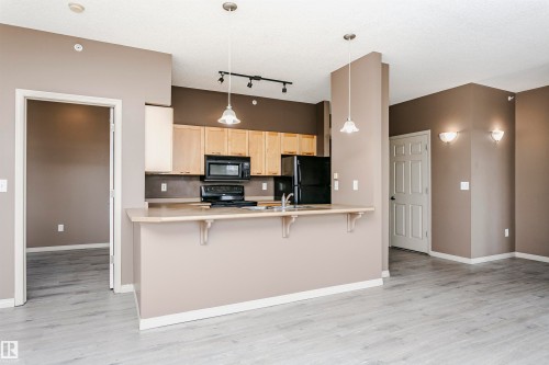 Open-concept kitchen with light wood cabinetry, black appliances, and a breakfast bar - 1-402 4245 139 Avenue, Edmonton, AB - Indoor Photo Showing Kitchen