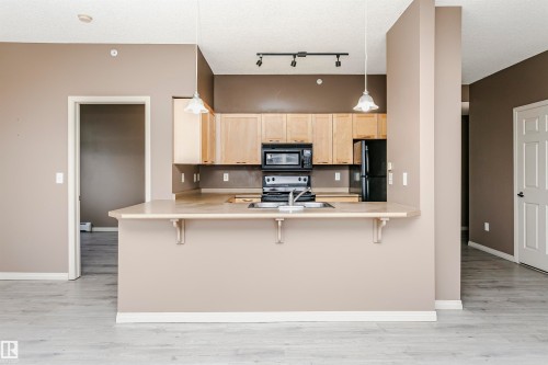 Kitchen featuring light wood cabinetry, black appliances, a peninsula with seating space, and wood-finish flooring - 1-402 4245 139 Avenue, Edmonton, AB - Indoor Photo Showing Kitchen