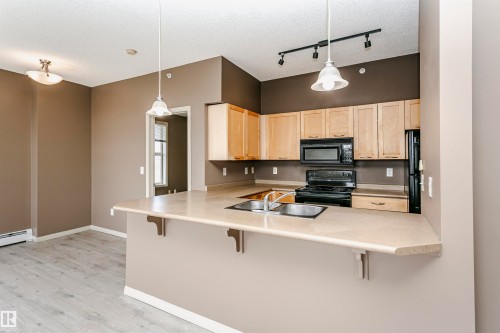 Open-concept kitchen with light wood-finish cabinetry, black appliances, and a breakfast bar with pendant lighting - 1-402 4245 139 Avenue, Edmonton, AB - Indoor Photo Showing Kitchen With Double Sink