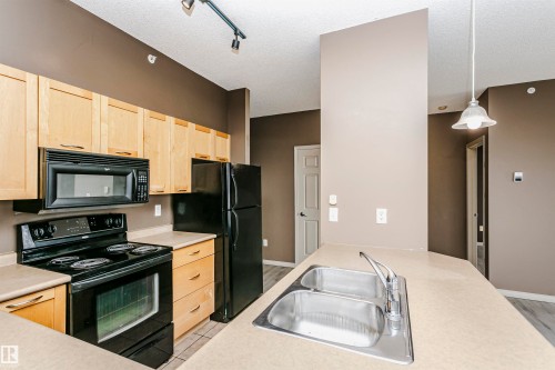 Kitchen featuring light wood-finish cabinetry, black appliances including a range and microwave, a double basin stainless steel sink, and light-toned countertops - 1-402 4245 139 Avenue, Edmonton, AB - Indoor Photo Showing Kitchen With Double Sink