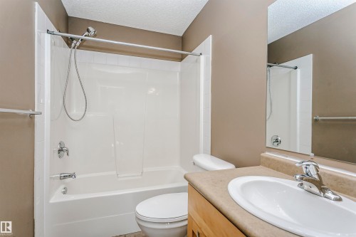 Bathroom featuring a combination shower and tub with white surround, a toilet, an integrated sink vanity with a light-toned countertop, and a wall-mounted mirror - 1-402 4245 139 Avenue, Edmonton, AB - Indoor Photo Showing Bathroom
