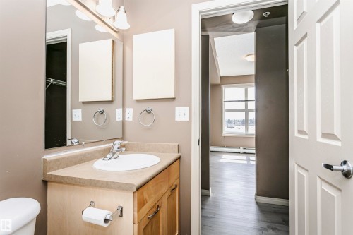 Bathroom vanity featuring a light wood-finish cabinet with silver hardware, an integrated sink, and a light-toned countertop - 1-402 4245 139 Avenue, Edmonton, AB - Indoor Photo Showing Bathroom