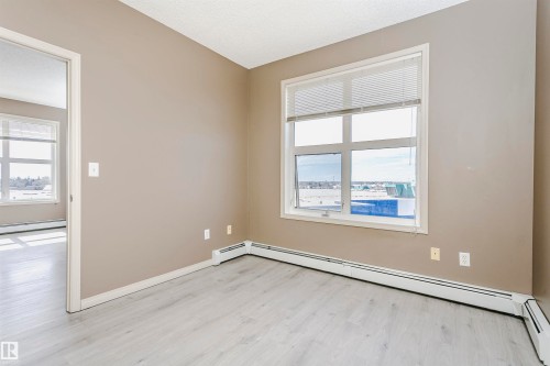 Spacious room featuring wood-finish flooring, a large window with horizontal blinds, and baseboard heating - 1-402 4245 139 Avenue, Edmonton, AB - Indoor Photo Showing Other Room