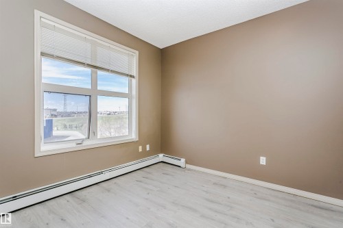 Room featuring wood-finish flooring, neutral wall paint, and a large window with horizontal blinds - 1-402 4245 139 Avenue, Edmonton, AB - Indoor Photo Showing Other Room