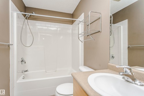 Full bathroom featuring a white tub and shower combination with chrome fixtures, a white toilet, and a vanity with an integrated sink and chrome faucet - 1-402 4245 139 Avenue, Edmonton, AB - Indoor Photo Showing Bathroom
