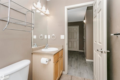 Bathroom vanity with a surface-mounted sink, light wood-finish cabinetry, and a mirrored wall - 1-402 4245 139 Avenue, Edmonton, AB - Indoor Photo Showing Bathroom
