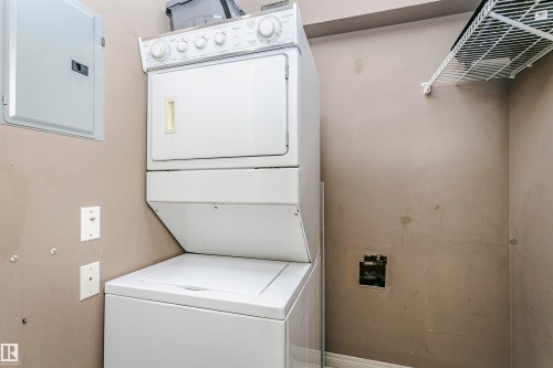 Dedicated laundry area featuring a stacked washer and dryer unit, white wire shelving, and a wall-mounted electrical panel - 1-402 4245 139 Avenue, Edmonton, AB - Indoor Photo Showing Laundry Room