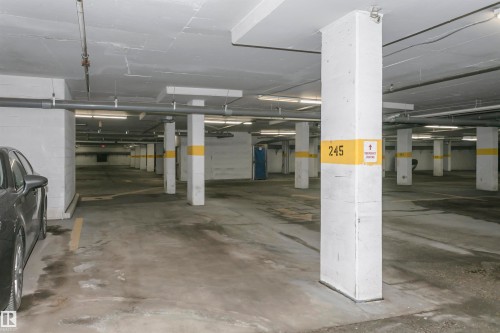 Underground parking garage featuring concrete flooring, structural support pillars, overhead lighting, and exposed utility piping - 1-402 4245 139 Avenue, Edmonton, AB - Indoor Photo Showing Garage