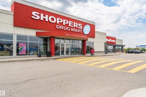 Commercial storefront featuring a prominent red facade with large white lettering, extensive window displays, and a wide paved parking area with yellow crosswalk markings - 1-402 4245 139 Avenue, Edmonton, AB - Outdoor