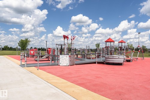 Modern playground featuring red cushioned surfacing, multiple play structures with red accents, accessible ramps, and integrated slides - 1-402 4245 139 Avenue, Edmonton, AB - Outdoor With View