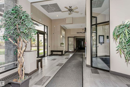 Building entryway featuring neutral-toned walls, high ceilings, and mixed flooring with wood-finish tile and carpet runners - 1-402 4245 139 Avenue, Edmonton, AB - Indoor Photo Showing Other Room