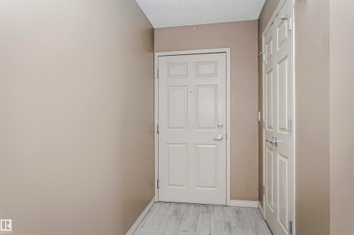 Entryway featuring light wood-finish flooring, neutral-toned walls, a white paneled door, and a white paneled closet door with silver-tone hardware - 1-402 4245 139 Avenue, Edmonton, AB - Indoor Photo Showing Other Room