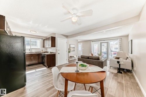 Open concept living space featuring a kitchen with dark cabinetry and a black refrigerator, a dining area with a round wooden table, and a living area with light-colored walls and double glass doors - 10327 150 Street, Edmonton, AB - Indoor