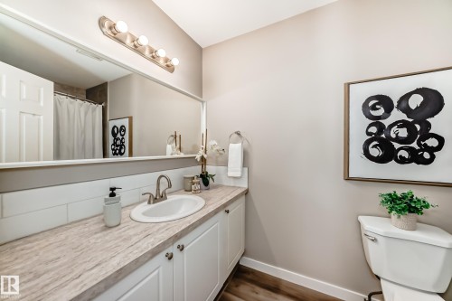 The bathroom features a vanity with a white countertop and white cabinetry, a large mirror, and a toilet - 10327 150 Street, Edmonton, AB - Indoor Photo Showing Bathroom