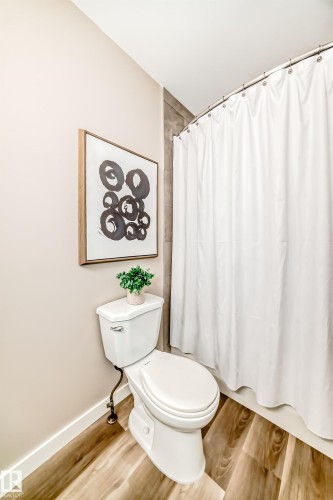 The bathroom features wood-look flooring, a white toilet, and a white shower curtain - 10327 150 Street, Edmonton, AB - Indoor Photo Showing Bathroom