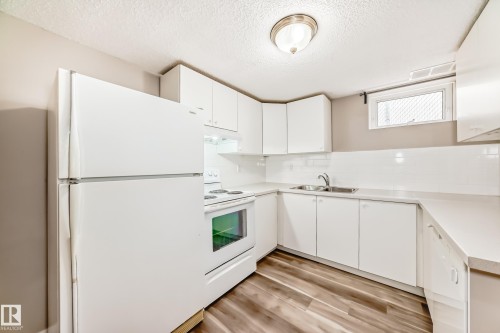 Kitchen featuring white cabinetry, white appliances, light countertops, and wood-style flooring - 10327 150 Street, Edmonton, AB - Indoor Photo Showing Kitchen With Double Sink
