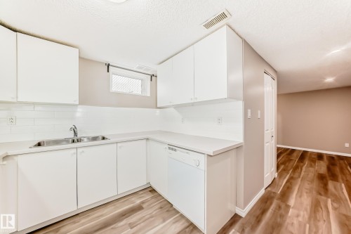 The kitchen features white cabinetry, a white countertop, a double sink, and a white dishwasher - 10327 150 Street, Edmonton, AB - Indoor Photo Showing Kitchen With Double Sink