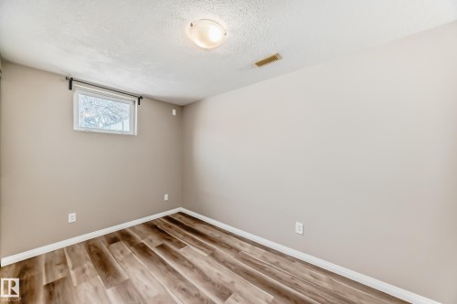 This room features wood-look flooring, light-colored walls, and a window with a black curtain rod - 10327 150 Street, Edmonton, AB - Indoor Photo Showing Other Room