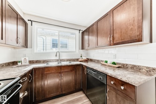 This kitchen features rich wood cabinetry, a double basin sink, a modern subway tile backsplash, and durable countertops - 10327 150 Street, Edmonton, AB - Indoor Photo Showing Kitchen With Double Sink