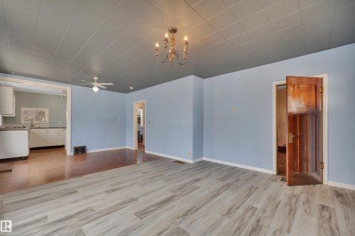 Spacious room featuring light blue walls, wood-finish flooring, and a decorative ceiling fixture - 4907 48 Avenue, Leduc, AB - Indoor