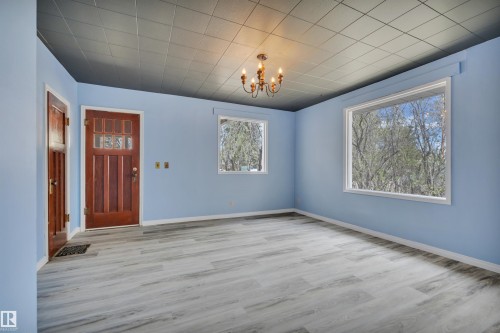 Entry area featuring a solid wood door with glass inserts, wood-finish flooring, two large windows, and a brass chandelier - 4907 48 Avenue, Leduc, AB - Indoor Photo Showing Other Room