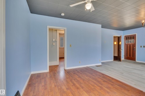 Interior space featuring a mix of wood-finish flooring and light-toned plank flooring, light blue wall finishes, and a gray acoustic tile ceiling with an attached ceiling fan - 4907 48 Avenue, Leduc, AB - Indoor Photo Showing Other Room