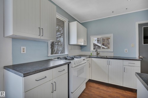 Kitchen featuring white cabinetry with dark hardware, dark countertops, white subway tile backsplash, and a white gas range - 4907 48 Avenue, Leduc, AB - Indoor Photo Showing Kitchen With Double Sink