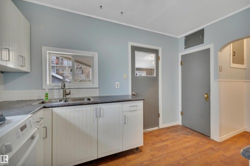 Kitchen featuring white cabinetry, dark countertops, wood-finish flooring, and a stainless steel double sink - 4907 48 Avenue, Leduc, AB - Indoor Photo Showing Kitchen With Double Sink