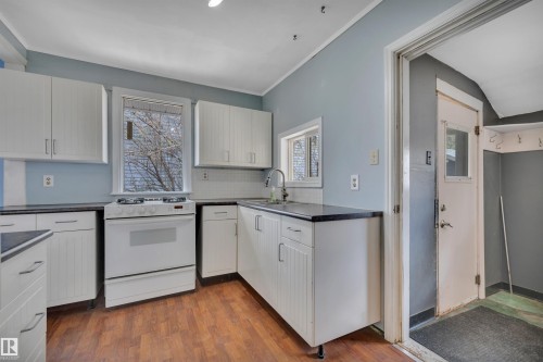 Kitchen featuring white cabinetry, dark countertops, a white gas range, and wood-finish flooring - 4907 48 Avenue, Leduc, AB - Indoor Photo Showing Kitchen