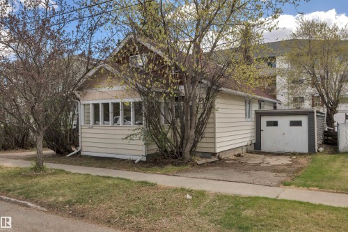 Single-family residence featuring a front sunroom with multiple windows, light-colored siding, and a detached single-car garage with a white overhead door - 4907 48 Avenue, Leduc, AB - Outdoor