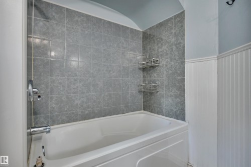 Bathtub and shower surround featuring square gray wall tiles and chrome fixtures - 4907 48 Avenue, Leduc, AB - Indoor Photo Showing Bathroom