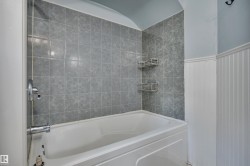 Bathtub and shower surround featuring square gray wall tiles and chrome fixtures - 