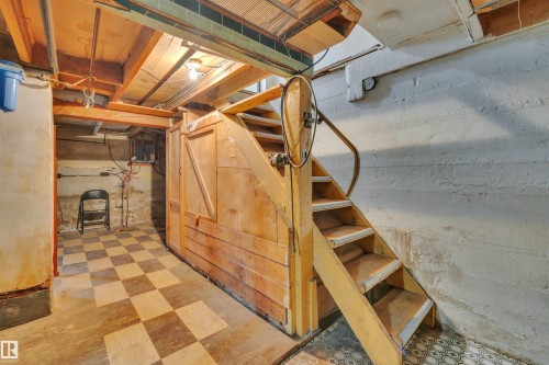 Basement area featuring a wooden staircase with a built-in storage compartment, exposed ceiling joists, and a checkered floor pattern - 4907 48 Avenue, Leduc, AB - Indoor