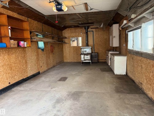 Garage space featuring concrete flooring, built-in shelving, wood-finish wall panels, and a utility sink with cabinetry - 4907 48 Avenue, Leduc, AB - Indoor Photo Showing Garage