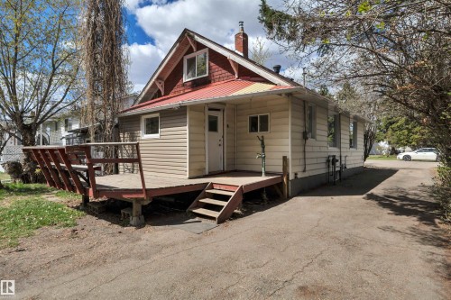 Property exterior featuring a red metal roof, beige siding, and a wooden deck with steps - 4907 48 Avenue, Leduc, AB - Outdoor With Exterior