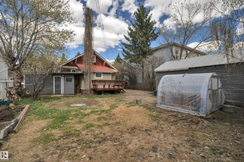 Rear exterior featuring a red metal roof, a wooden deck, and an attached storage shed - 4907 48 Avenue, Leduc, AB - Outdoor