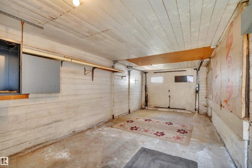 Enclosed garage space featuring a concrete floor, horizontal plank walls, a plank ceiling, and a built-in wall shelf - 4907 48 Avenue, Leduc, AB - Indoor Photo Showing Garage