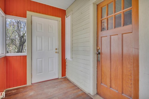 Enclosed porch area featuring wood-finish flooring, a white paneled door, and a traditional wood entry door with multiple glass panes - 4907 48 Avenue, Leduc, AB - Indoor Photo Showing Other Room