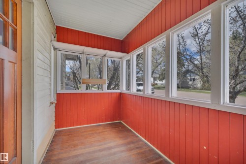Enclosed porch featuring wood-finish flooring, vibrant red vertical paneling, white trim, and multiple windows - 4907 48 Avenue, Leduc, AB - Indoor Photo Showing Other Room