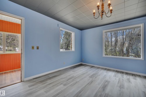 Spacious room featuring light blue walls, gray wood-finish flooring, a classic chandelier light fixture, and two large windows providing natural light - 4907 48 Avenue, Leduc, AB - Indoor Photo Showing Other Room