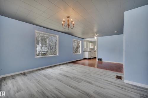 Spacious interior featuring light blue walls, wood-finish flooring, and a decorative chandelier - 4907 48 Avenue, Leduc, AB - Indoor