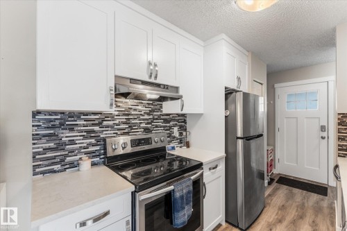 Contemporary kitchen featuring white cabinetry, a linear mosaic tile backsplash, and light-toned countertops - 35 Mcleod Place, Edmonton, AB - Indoor Photo Showing Kitchen With Stainless Steel Kitchen