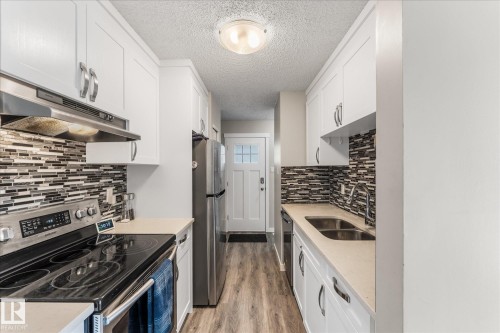 Galley kitchen featuring white shaker-style cabinetry, a mosaic tile backsplash, stainless steel appliances, and wood-finish flooring - 35 Mcleod Place, Edmonton, AB - Indoor Photo Showing Kitchen With Stainless Steel Kitchen With Double Sink With Upgraded Kitchen