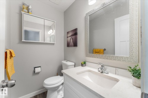 Bathroom featuring a vanity with an integrated sink and light-toned countertop, a decorative framed mirror, a medicine cabinet, a white toilet, and wood-finish flooring - 35 Mcleod Place, Edmonton, AB - Indoor Photo Showing Bathroom