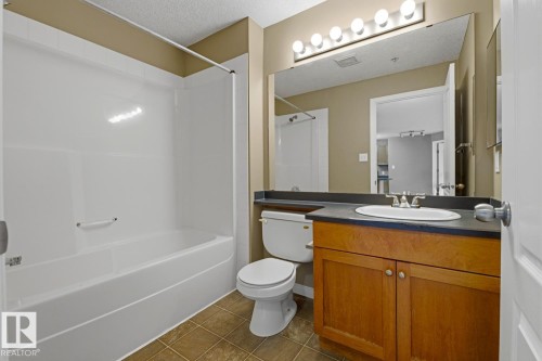 Full bathroom featuring a white tub/shower combination, a wood-finish vanity with a dark countertop, an integrated sink, a large wall-mounted mirror, and vanity lighting - 5106 7335 South Terwillegar Drive, Edmonton, AB - Indoor Photo Showing Bathroom