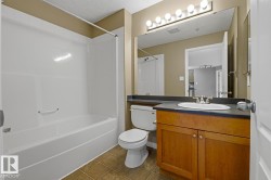 Full bathroom featuring a white tub/shower combination, a wood-finish vanity with a dark countertop, an integrated sink, a large wall-mounted mirror, and vanity lighting - 