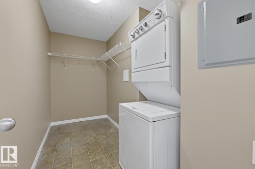 Dedicated laundry area featuring a white stacked washer and dryer, tile flooring, and integrated wire shelving - 5106 7335 South Terwillegar Drive, Edmonton, AB - Indoor Photo Showing Laundry Room