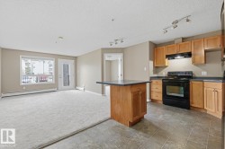 Open-concept kitchen and living area featuring light wood cabinetry, dark countertops, black appliances, and track lighting - 